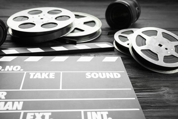 Movie clapper, camera lens and film reels on black wooden table, closeup