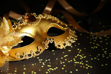 Beautiful carnival mask, ribbon and confetti on dark background, closeup