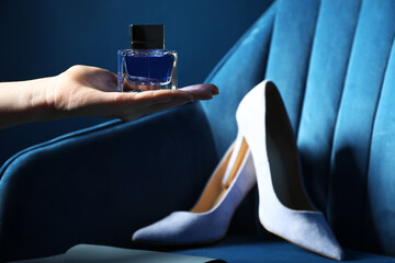 Woman holding bottle of perfume near armchair with high-heeled shoes, closeup