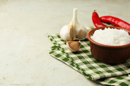 Sea salt in bowl, garlic and chili peppers on grey table, closeup. Space for text