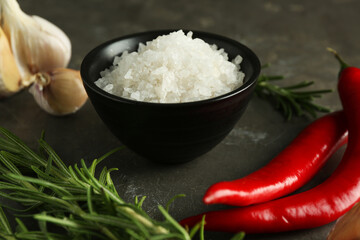 Sea salt in bowl, rosemary, chili peppers and garlic on grey table, closeup