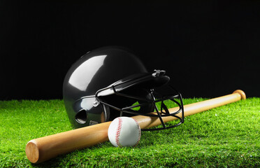 Baseball helmet, bat and ball on artificial grass against black background