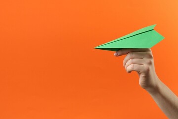 Woman with green paper plane on orange background, closeup. Space for text