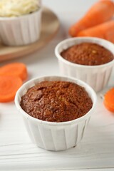 Tasty carrot muffins with cream and fresh vegetable on white wooden table, closeup
