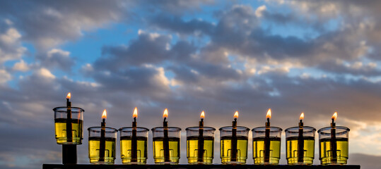Hanukkah design. Image depicts Jewish Holiday of Miracle Light – Hanukkah, selected focus on menorah with olive oil burning candles, blurred cloud  background. No AI tools were used