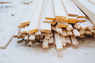 A stack of wooden planks covered in fresh white snow symbolizes essential building materials, perfect for construction and home improvement themes in a serene winter setting