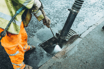 Road Workers cleaning a storm drain using pressure washer on a rainy day in an urban area
