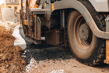 Fototapeta premium Construction crew laying asphalt on a new road in a residential area during daylight hours
