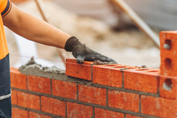 Builder constructs a red brick wall using mortar and precise hand placement on a construction site