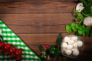 Wooden table decorated with tomatoes, mushrooms, spinach, mozzarella, basil and spices. Place for dish pizza pasta potatoes on a wooden table, top view