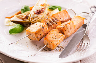 Traditional grilled salmon skewer with chicory salad, carrots and bechamel sauce served as close-up on a classic design plate