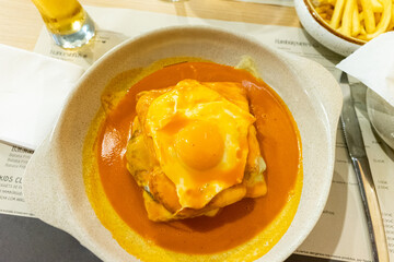 Traditional Portuguese Francesinha sandwich served on a restaurant table, topped with melted cheese and savory sauce, capturing authentic Porto cuisine and dining culture.