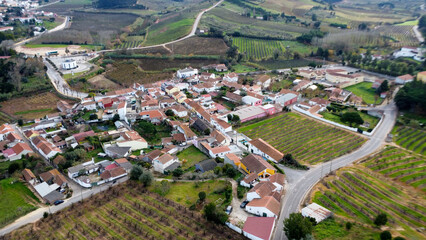 Vista de uma aldeia rural capturada por um drone. A cena apresenta pequenas casas com arquitetura tradicional, espalhadas por uma paisagem verdejante e exuberante, entrelaçada por estradas 