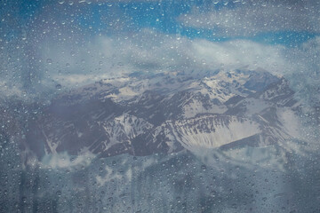 A beautiful mountain landscape of the Alps with snow behind wet, foggy glass