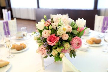 Beautiful table setting with tableware, flowers, accessories and beautiful rose for a party, wedding reception or holiday event. Photographed in ambiental light.