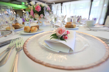 Beautiful table setting with tableware, flowers, accessories and beautiful rose for a party, wedding reception or holiday event. Photographed in ambiental light.