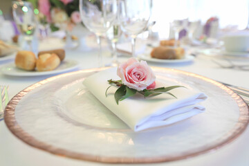 Beautiful table setting with tableware, flowers, accessories and beautiful rose for a party, wedding reception or holiday event. Photographed in ambiental light.