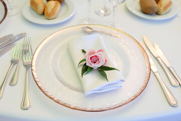 Beautiful table setting with tableware, flowers, accessories and beautiful rose for a party, wedding reception or holiday event. Photographed in ambiental light.