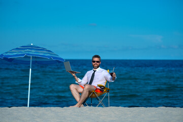 Business vacation. Handsome businessman on summer vacation. Businessman rest on sea beach holding...