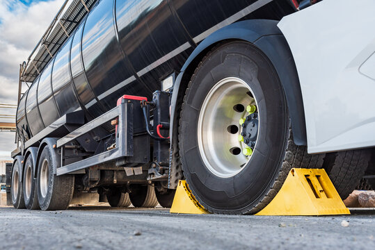 Wheel chocks placed on the drive wheel of a tanker truck to immobilize it for safety during the loading or unloading processes.