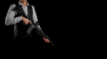 A man in a formal outfit, consisting of a white shirt and a grey vest, is holding a black assault rifle against a dark background.