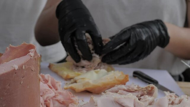 Cooking trendy Italian panini sandwich with focaccia or ciabatta. Slicing salami, mortadella, and ham.Pesto, pistachio sauces and stracciatella cheese. Street food gastronomic festival.