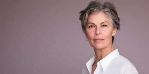 Sophisticated mature woman posing in studio, wearing white shirt against soft lilac backdrop