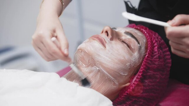 A cosmetologist applying anesthesia cream to a woman's face before a treatment. Concept of rejuvenation and anti-aging skin care. Perfect for content about cosmetic and anti-aging procedures.