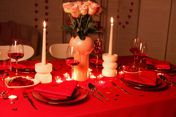 Dining table with setting, burning candles and pink roses for Valentine's Day celebration in evening