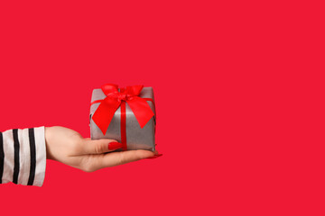 Female hand holding gift box on red background. Valentine's Day celebration