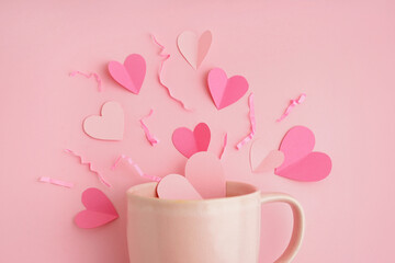 Cup with hearts and shredded paper on pink background. Valentine's Day celebration