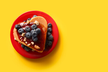 Plate with tasty pancakes in shape of heart, blueberry and nuts on yellow background. Valentine's Day celebration