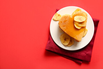 Plate with tasty pancakes in shape of heart, dried banana and honey on red background. Valentine's Day celebration
