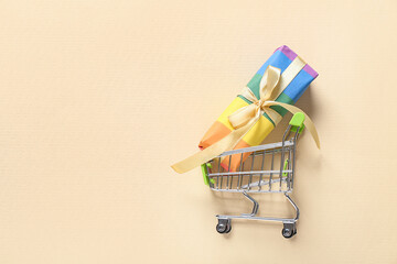 Small shopping cart with rainbow LGBT gift box on beige background. Valentine's Day celebration