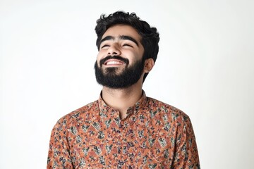 Happy young man from Arabia or India bearded in a casual shirt standing against a plain white background holding a laptop glancing to the side smiling blissfully lost in thoug