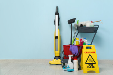 Janitor's trolley with cleaning supplies and caution sign near blue wall