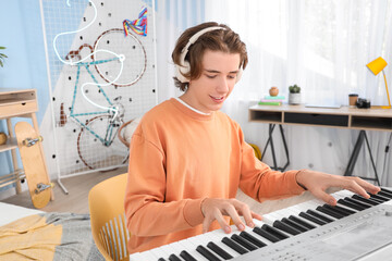 Male student with headphones playing synthesizer in bedroom