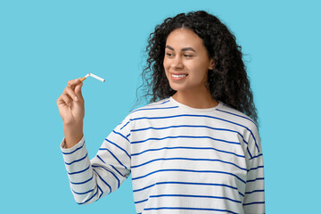 Happy young African-American woman with broken cigarette on blue background. Stop smoking concept