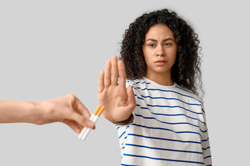 Young African-American woman rejecting cigarettes on grey background. Stop smoking concept