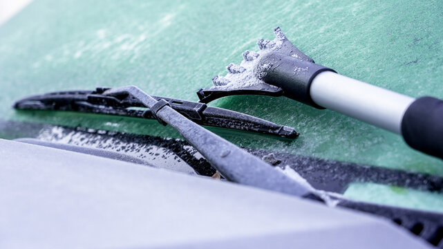 Winter car preparation in a snowy environment with a scraper clearing the windshield for safe driving