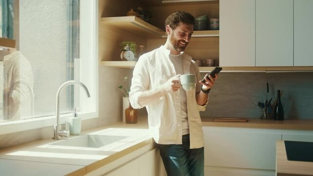 Man Checking Phone While Enjoying Coffee in Sunlit Kitchen
