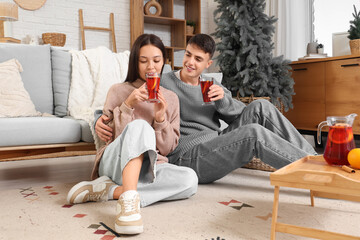 Happy couple with jug and glasses of delicious mulled wine on wooden tray sitting at home