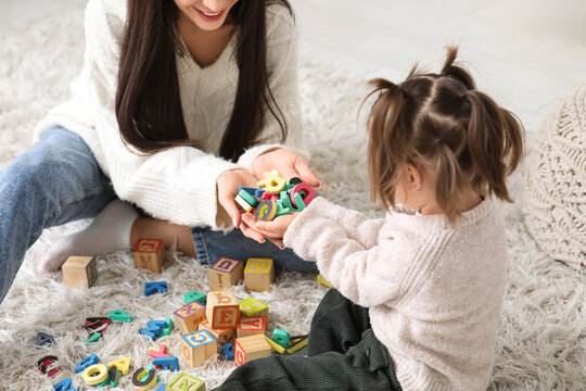 Cute little girl with teacher and letters learning alphabet on carpet at home