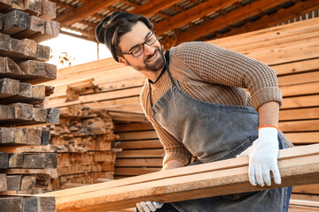 Male carpenter stacking wooden planks at sawmill