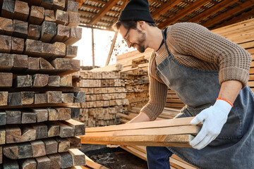Male carpenter stacking wooden planks at sawmill