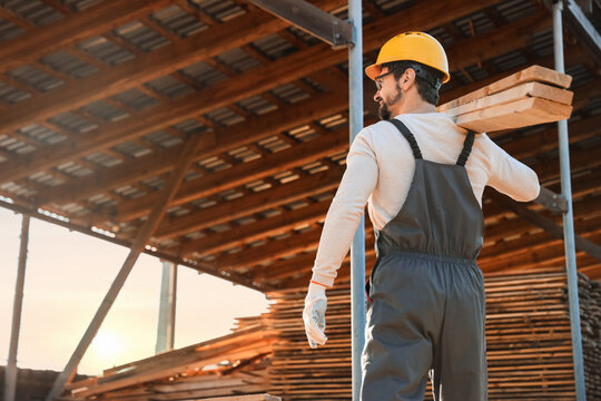 Male carpenter carrying wooden planks at sawmill, back view