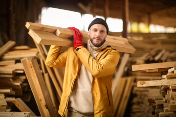 Male carpenter carrying wooden planks at sawmill