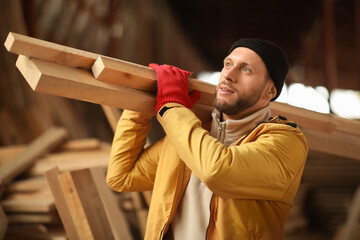 Male carpenter carrying wooden planks at sawmill