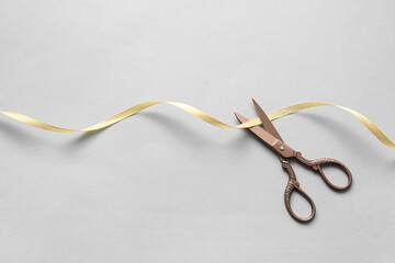 Beautiful satin ribbon with scissors on grey background