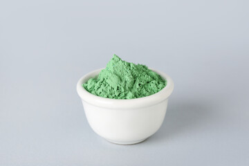 Bowl of green powder pigment on light background